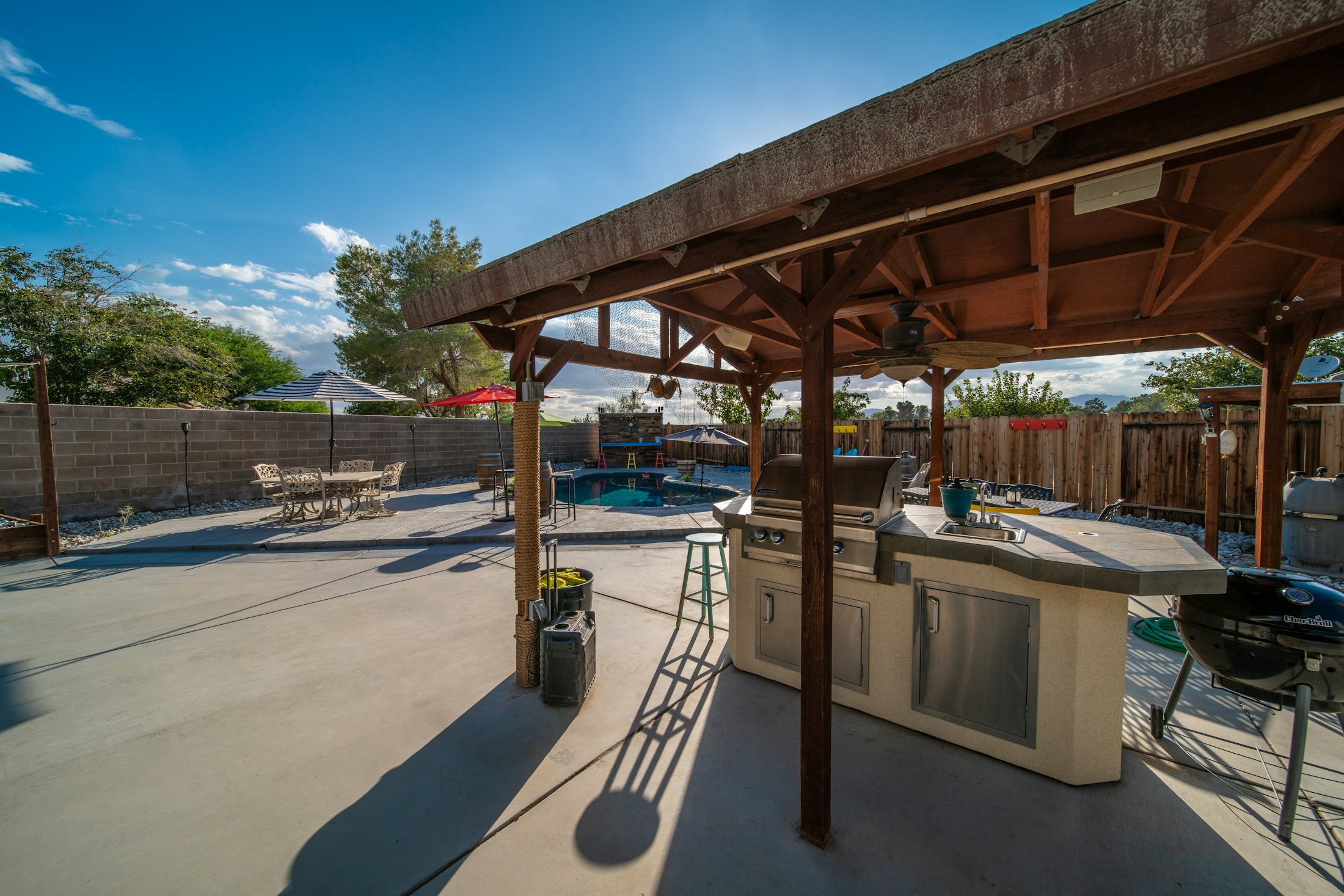 Wide concrete patio with an outdoor kitchen under a wood pergola beside a pool